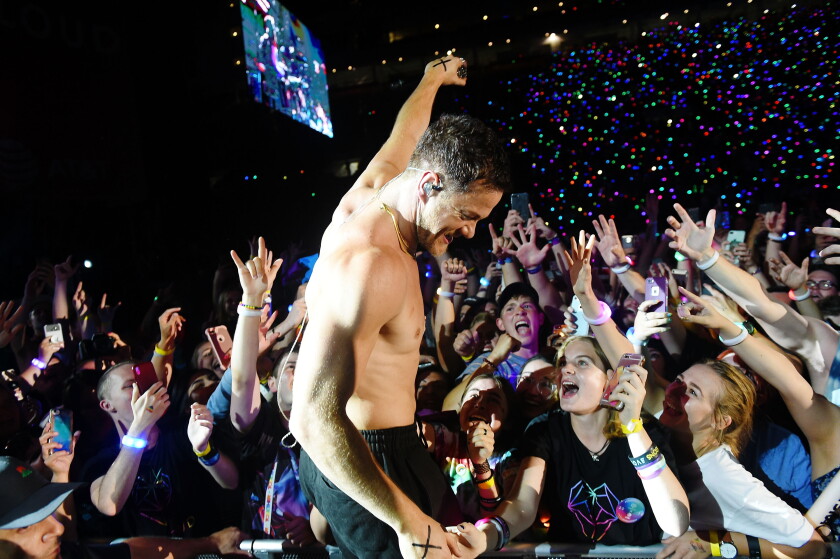 Dan Reynolds of Imagine Dragons performing at LOVELOUD Festival, surrounded by fans holding phones and light-up wristbands.