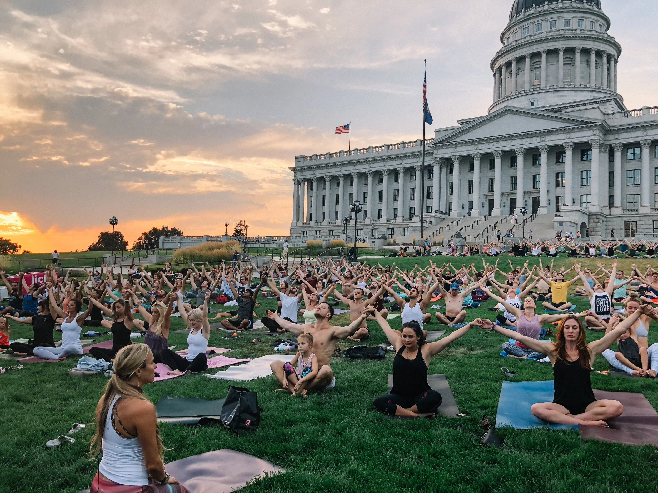 Hundreds of people doing yoga together on the lawn of the Utah State Capitol at sunset